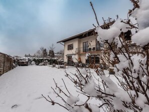 A two-story house with a balcony, surrounded by snow-covered ground and trees.