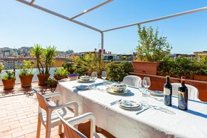 A rooftop terrace with a table set for dining, potted plants, and city views. - Terrazza 30 by Napoliapartments (Naples)