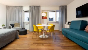 A modern hotel room with a bed, a blue sofa, a dining table with yellow chairs, and a TV mounted on the wall. - Guicciardini Apartment (Florence)