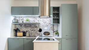 A compact kitchen with teal cabinets, a stainless steel range hood, a microwave, and a small countertop with a sink. - Guicciardini Apartment (Florence)
