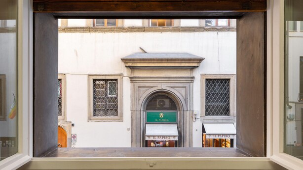 A view through a window of a building with a sign reading "IL PAPIRO" and a door with a metal gate. - Guicciardini Apartment (Florence)