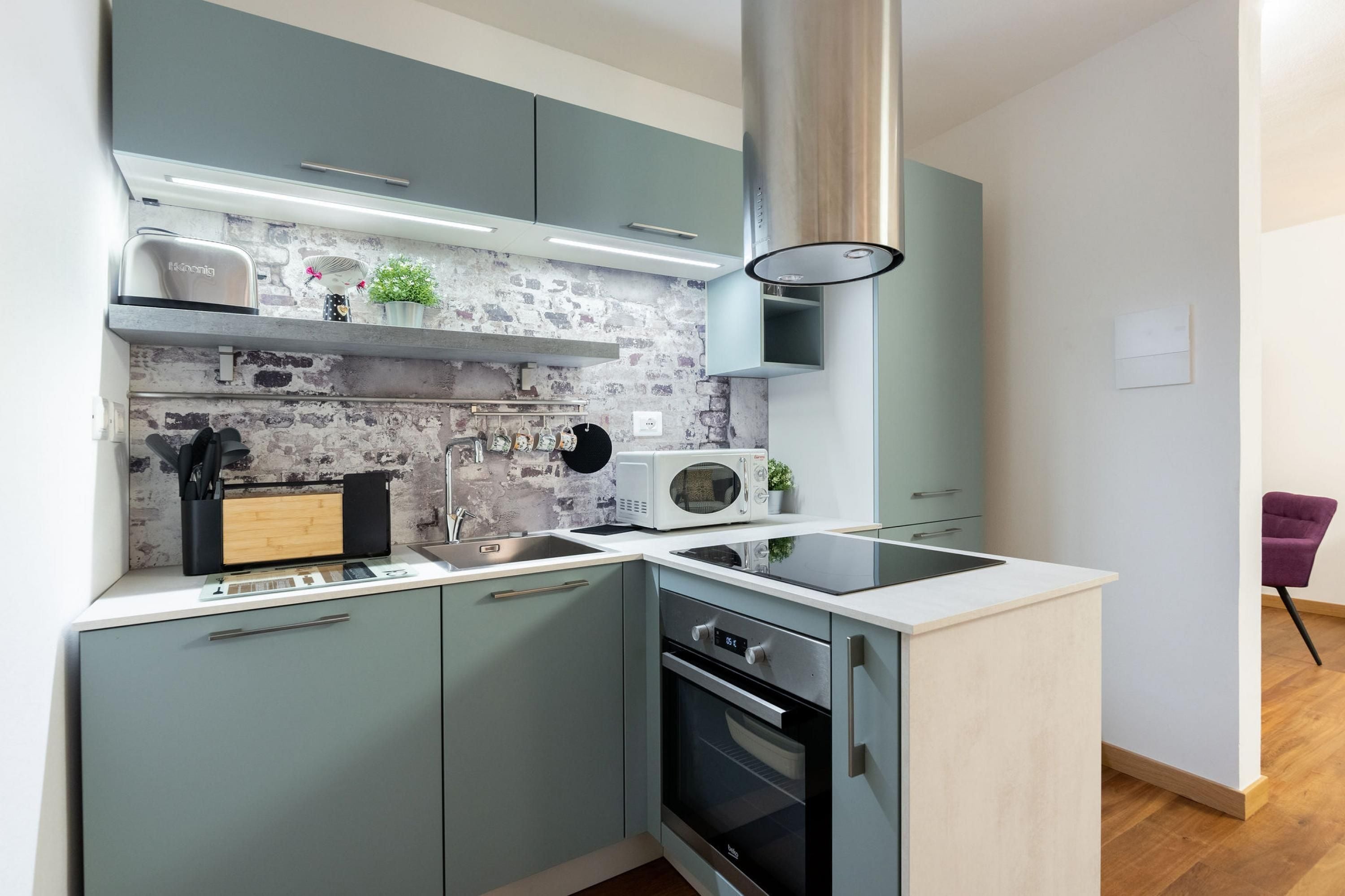 Una cocina moderna con armarios grises, un microondas integrado y un horno de acero inoxidable.
