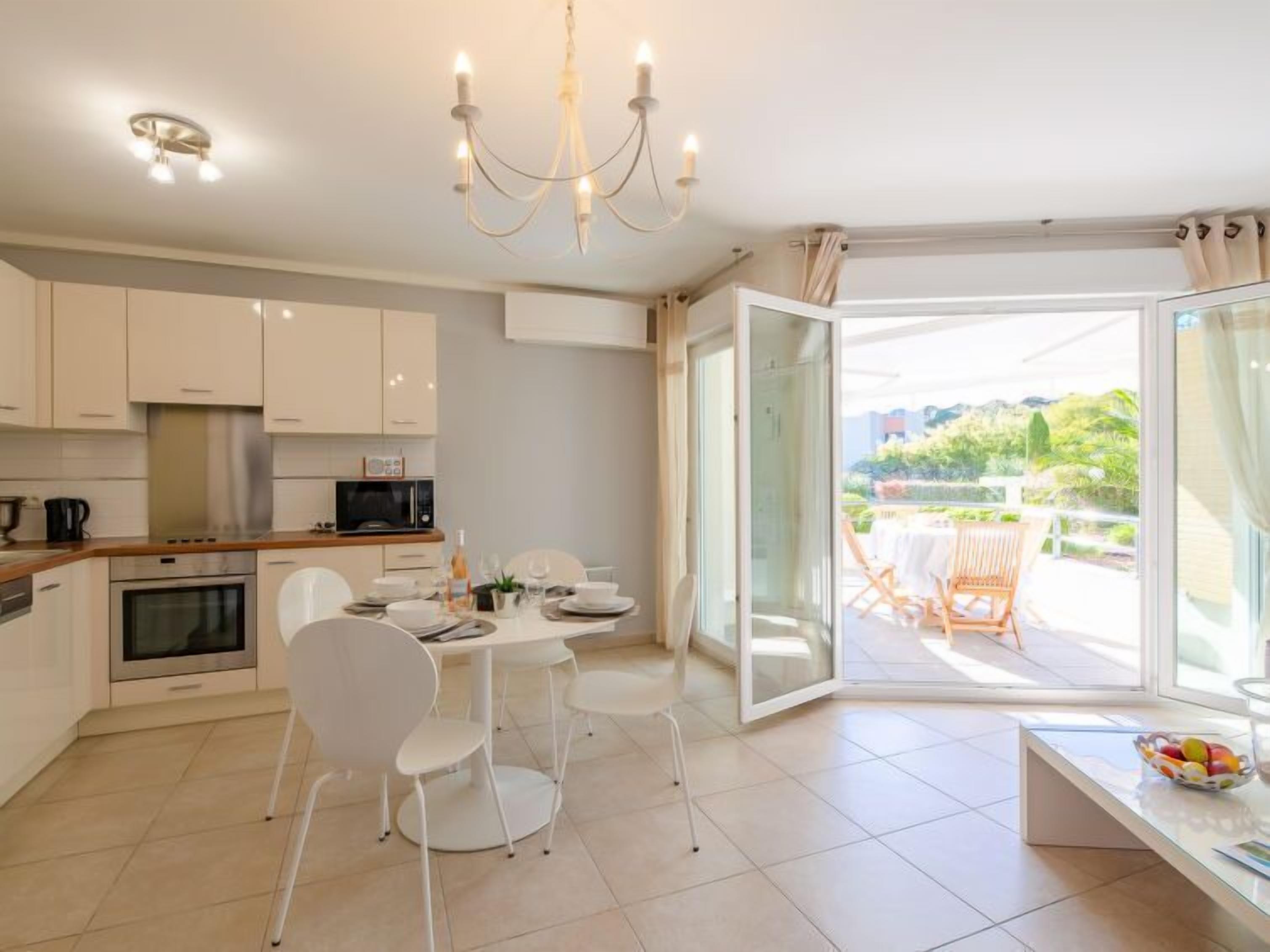 A modern kitchen with white cabinets, a dining area with white chairs, and a large sliding glass door leading to an outdoor patio.
