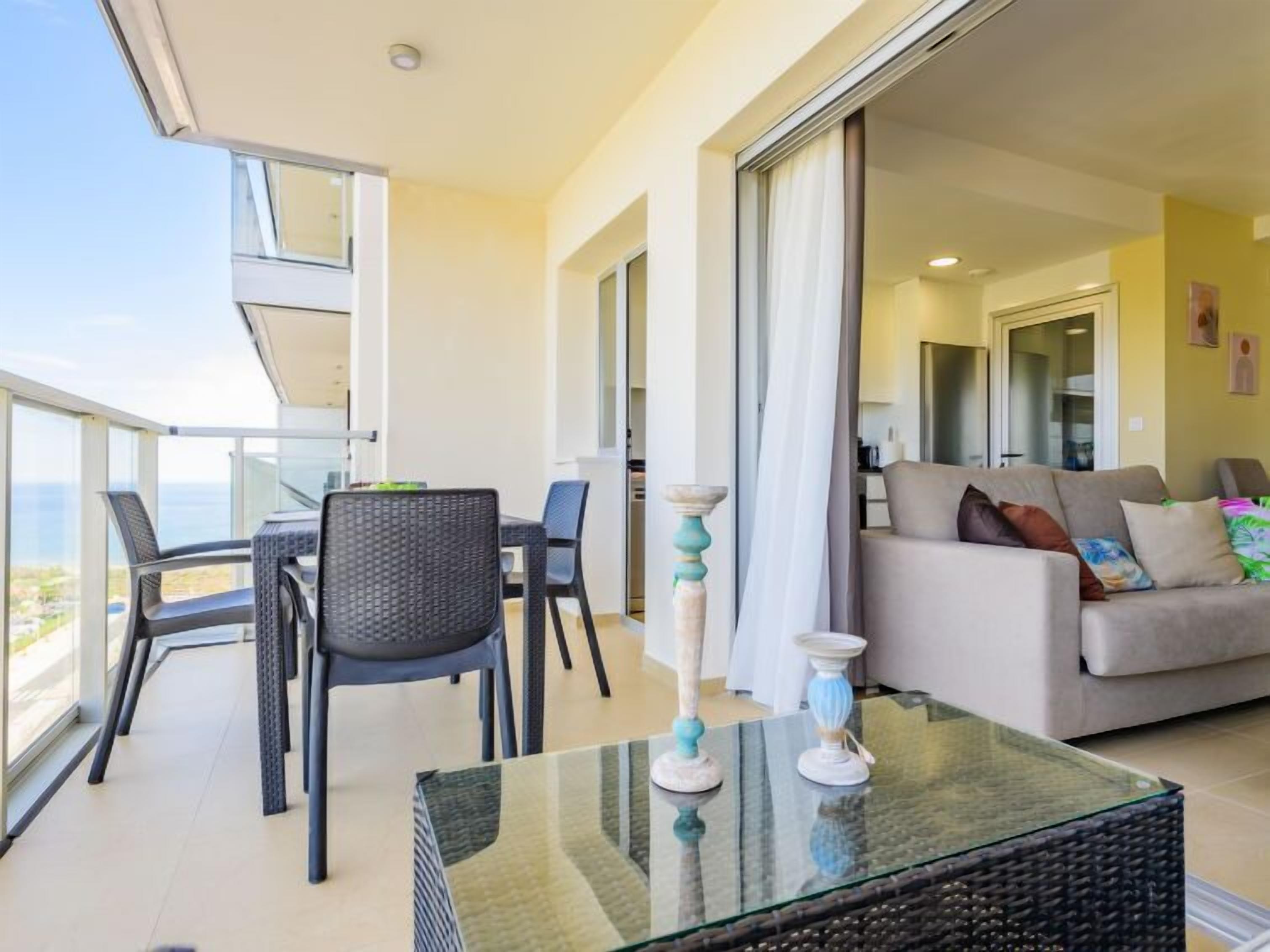 Ein Balkon mit Glastisch, Stühlen und einer Couch.