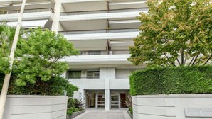 Un edificio de varios pisos con una entrada central, rodeado de vegetación y un camino empedrado.
