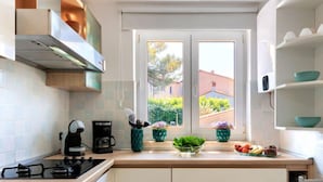 A modern kitchen with white cabinets, a gas stove, a coffee maker, and a window with a view of greenery and buildings.