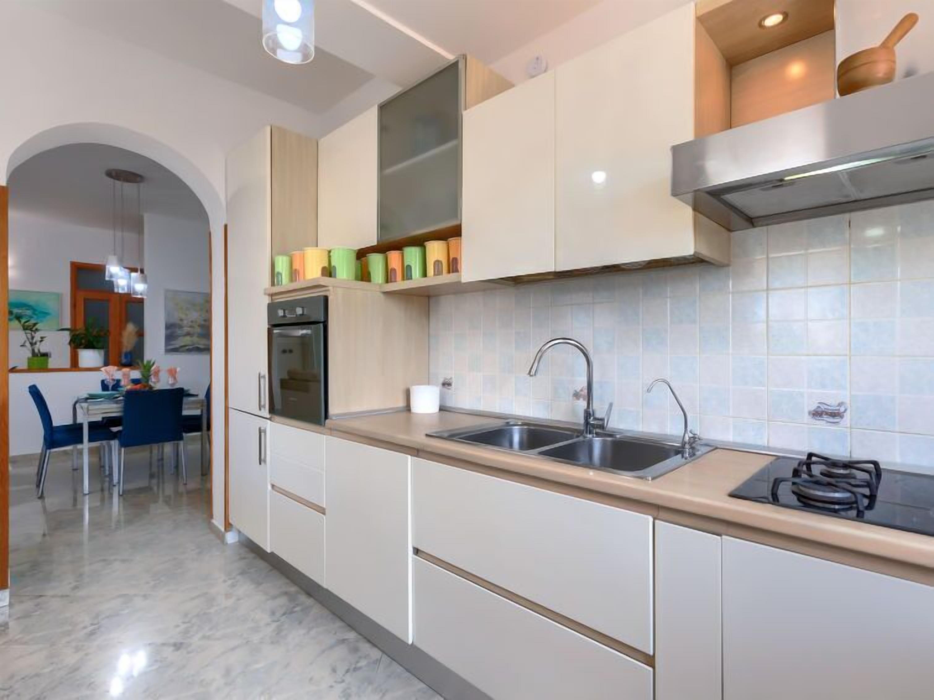 A modern kitchen with white cabinets, a double sink, and a built-in oven.