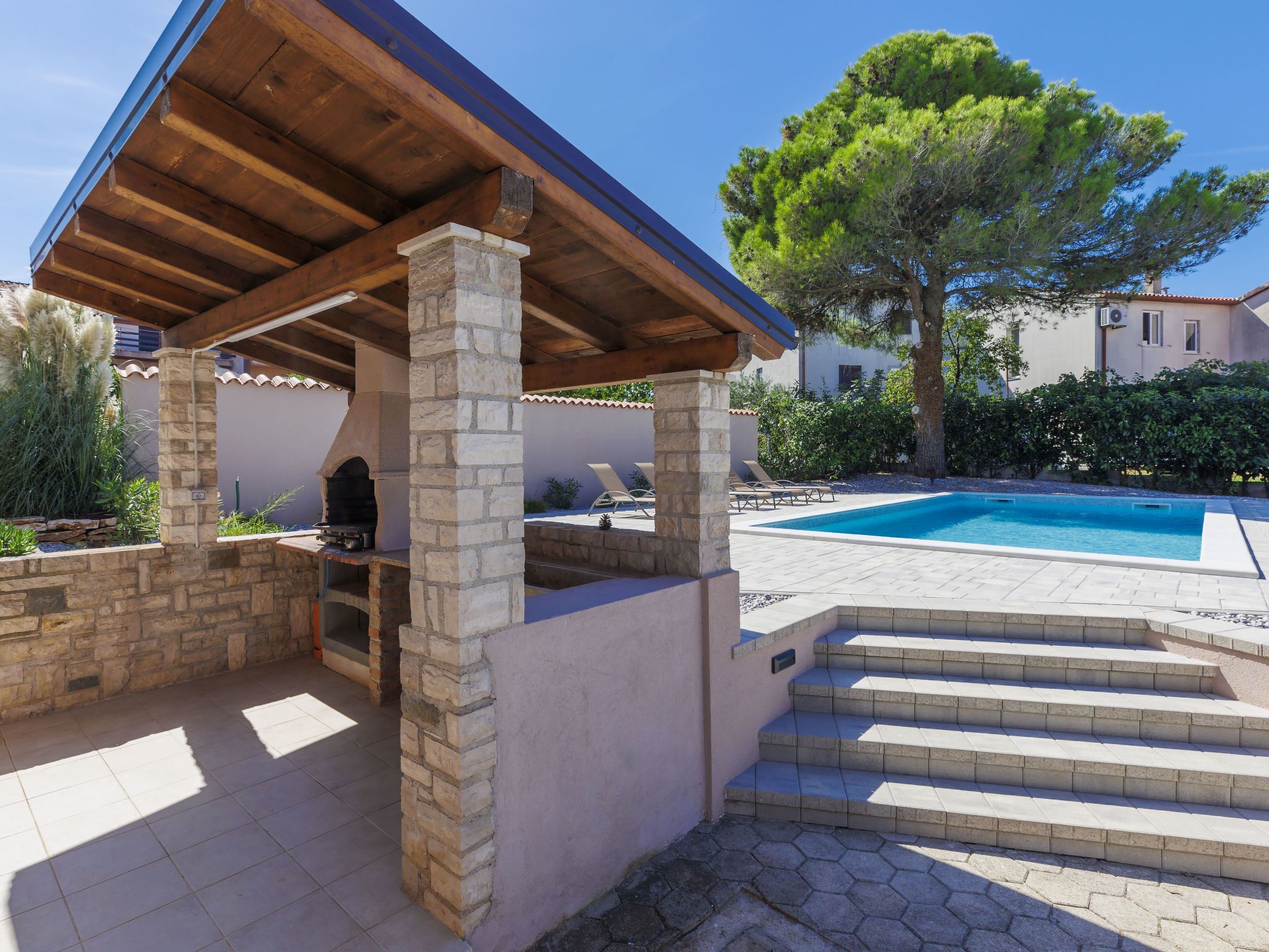 A stone barbecue area with a pool and steps leading to a poolside lounge.