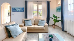 A modern living room with a beige sofa, a coffee table, and a large window with curtains.