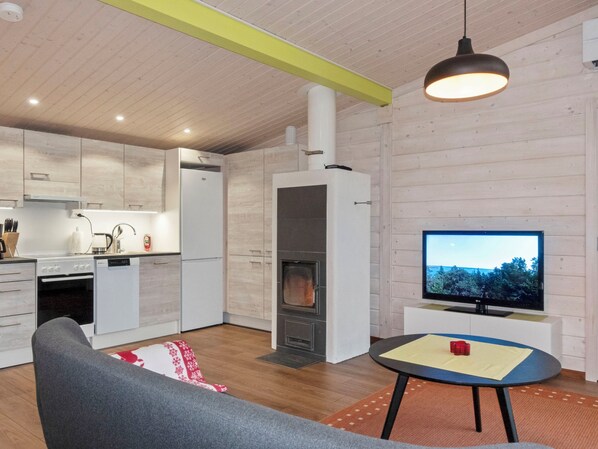 A modern kitchen with white cabinets, a built-in oven, and a stove. There's a dining area with a table and chairs, and a TV mounted on the wall.