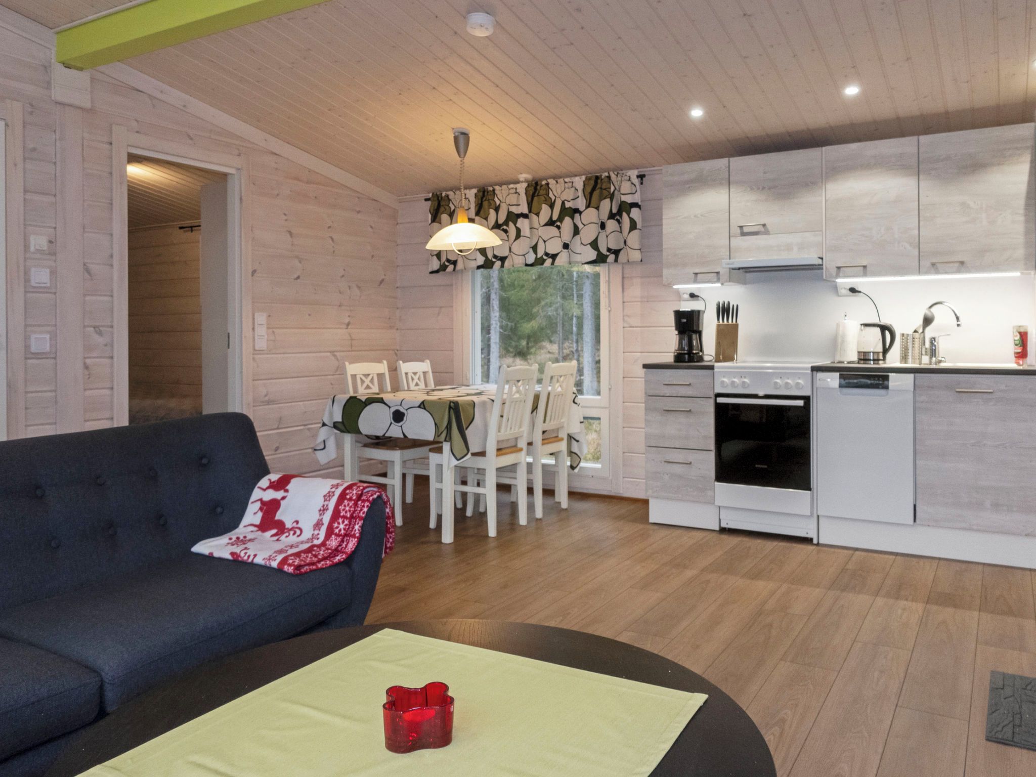 Un espacio de sala acogedor con un sofá y una mesa de comedor con sillas. Se observa una cocina con electrodomésticos modernos al fondo.