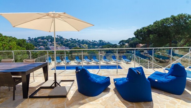 A rooftop terrace with a pool, blue lounge chairs, a table, and an umbrella. - Club Villamar - (Lloret de Mar)