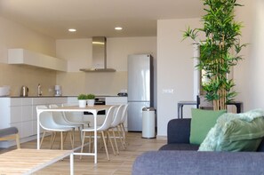 Una cocina moderna con armarios blancos, un refrigerador de acero inoxidable y un comedor con sillas blancas.