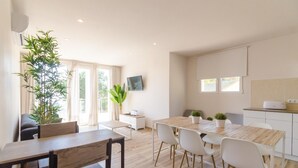 A modern kitchen with a dining area, featuring a wooden table and chairs, a small kitchen island, and a large potted plant. - Club Villamar - (Lloret de Mar)
