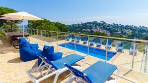 A rooftop pool area with blue lounge chairs, a table, and an umbrella. - Club Villamar - (Lloret de Mar)