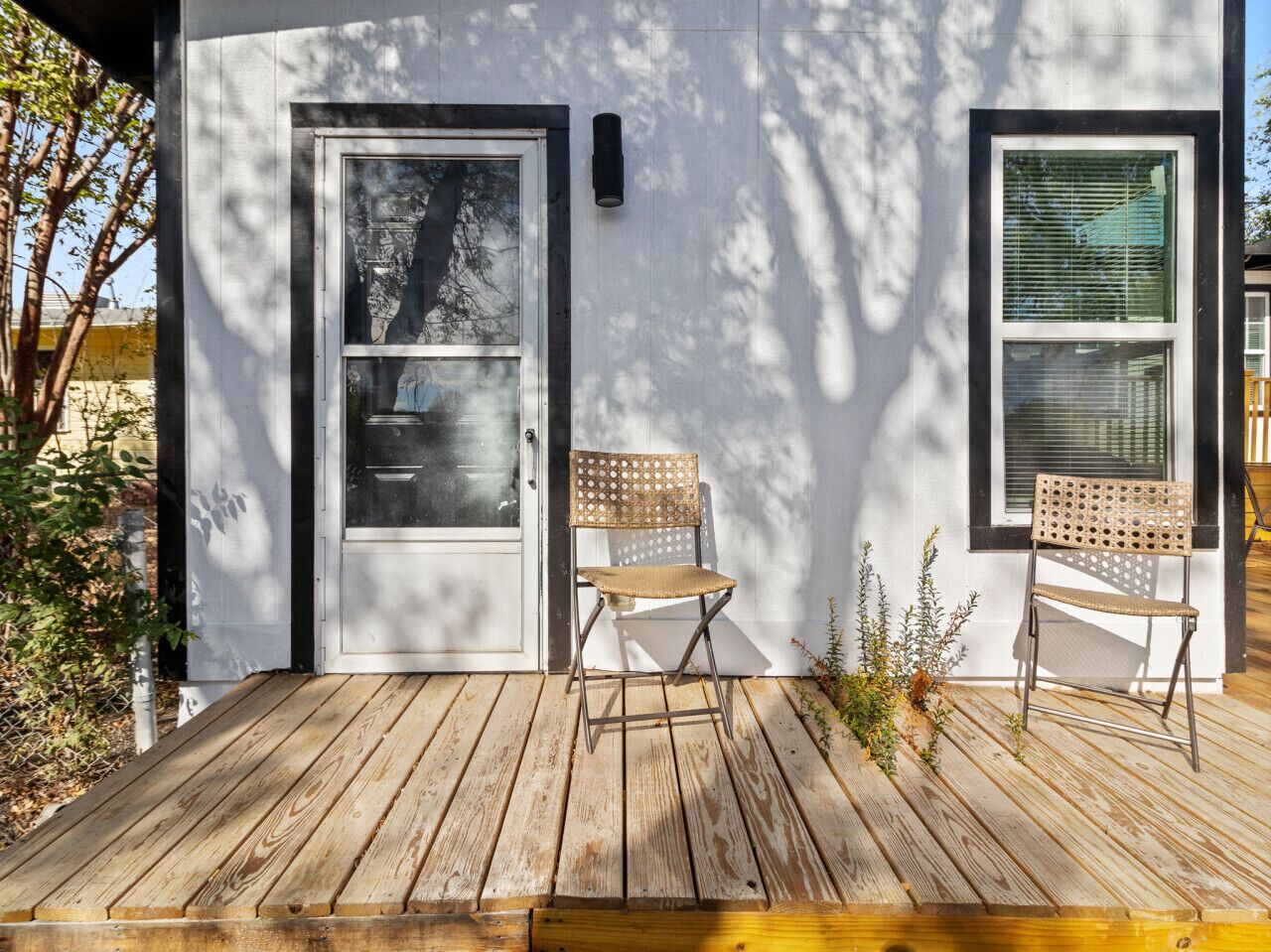 Eine Holzterrasse mit zwei Korbstühlen und einer Tür zu einem Gebäude.