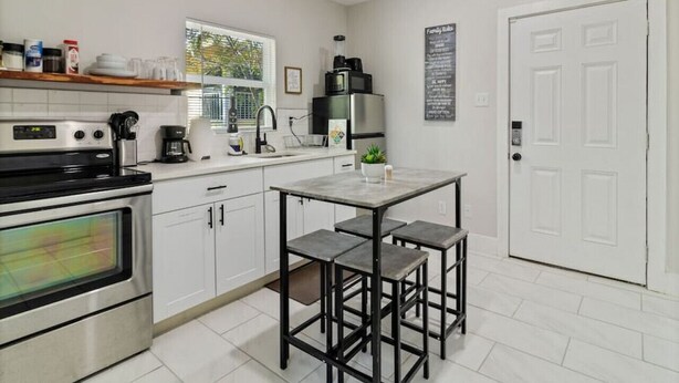 A modern kitchen with white cabinets, a built-in oven, a coffee maker, and a small island with stools.