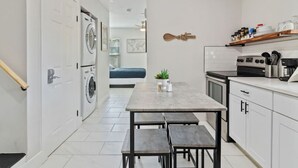 A compact kitchen with a dining table and benches, a washing machine, and a small dining area with a blue sofa.