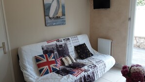 Ein gemütliches Wohnzimmer mit einer Couch, verziert mit einer Quilttdecke mit der Skyline von New York und Flaggen, einem Segelbootgemälde und einem kleinen Tisch mit einer Blumenvase.