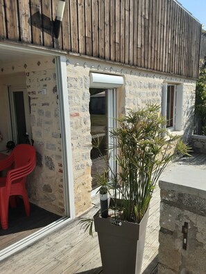 A stone building with a wooden roof, a red plastic chair, and a potted plant.