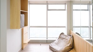 A room with a large window, a wooden bookshelf, a bean bag chair, and a radiator.