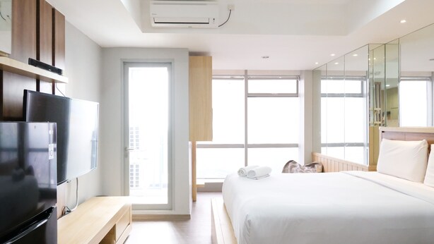 A modern hotel room with a bed, a TV, a desk, and a large window.