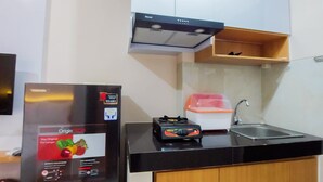 A compact kitchen with a black countertop, a built-in stove, a sink, and wooden cabinets. - Minimalist Studio Apartment At Serpong Garden (Cisauk)