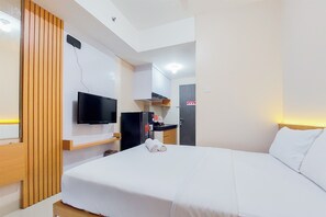 A hotel room with a bed, a TV mounted on the wall, a desk with a computer, and a door. - Minimalist Studio Apartment At Serpong Garden (Cisauk)