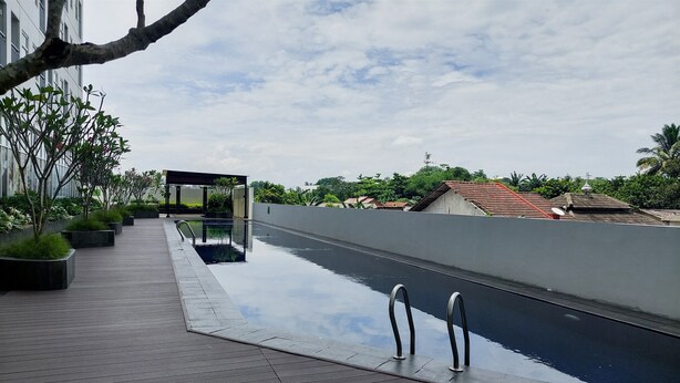 A rooftop pool with a wooden deck, surrounded by potted plants and a clear view of the cityscape. - Minimalist Studio Apartment At Serpong Garden (Cisauk)