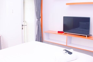 A hotel room with a bed, a TV on a stand, and a remote control on the bed.