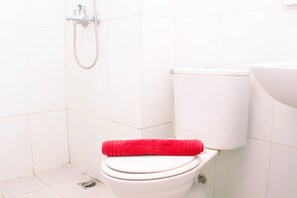 A white toilet with a red towel on the seat and a showerhead above it.