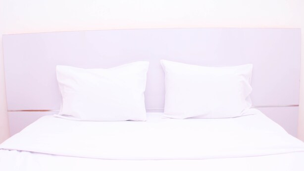 Una cama con ropa de cama y almohadas blancas, un cabecero y una pared lisa.