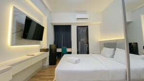 A modern hotel room with a large bed, a flat-screen TV mounted on the wall, a desk with a chair, a wardrobe, and an air conditioning unit. - Fully Furnished 1Br The Alton Apartment (Semarang)