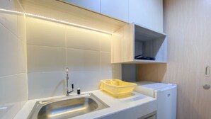 A modern kitchen with white cabinetry, a stainless steel sink, and a yellow dish rack. - Fully Furnished 1Br The Alton Apartment (Semarang)