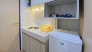 A compact kitchenette with a sink, a small refrigerator, and a shelf with kitchenware. - Fully Furnished 1Br The Alton Apartment (Semarang)
