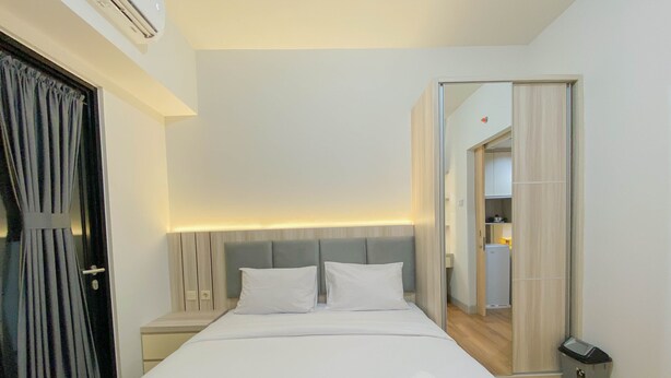 A modern hotel room with a large bed, two pillows, a nightstand, a mirror, and a small trash bin. - Fully Furnished 1Br The Alton Apartment (Semarang)