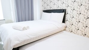 A neatly made bed with white linens and rolled towels, a black headboard, and a wall with a repeating pattern of Parisian landmarks. - Clean Studio With Connected To Mall At Orchard Supermall Mansion Apartment (Surabaya)