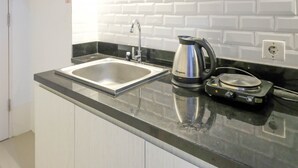 A kitchen with a stainless steel sink, a kettle, and an induction cooktop. - Clean Studio With Connected To Mall At Orchard Supermall Mansion Apartment (Surabaya)