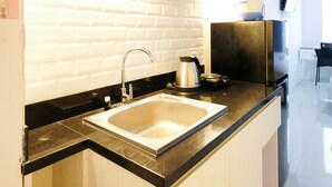 A modern kitchen with a stainless steel sink, black countertop, and white tiled backsplash. - Clean Studio With Connected To Mall At Orchard Supermall Mansion Apartment (Surabaya)