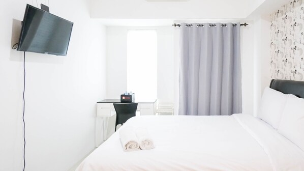 A hotel room with a bed, a desk with a computer, a TV mounted on the wall, and a window with curtains. - Clean Studio With Connected To Mall At Orchard Supermall Mansion Apartment (Surabaya)