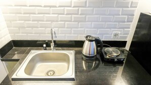 A kitchen with a stainless steel sink, a kettle, and a rice cooker on a black countertop. - Clean Studio With Connected To Mall At Orchard Supermall Mansion Apartment (Surabaya)