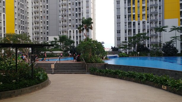 A residential building with a swimming pool, surrounded by greenery and a covered area with steps leading to the pool.