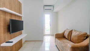 A modern living room with a flat-screen TV mounted on a wooden panel, a beige sofa, and a white shelf.