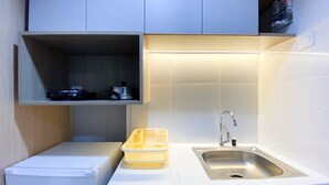 Una cocina compacta con refrigerador empotrado, un lavamanos y un estante sobre la encimera.