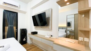 Una habitación de hotel moderna con televisión de pantalla plana montada en la pared, mesita de noche de madera, cama con ropa blanca, calefacción integrada y un espejo grande.