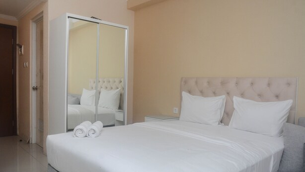 Una cama bien hecha con sábanas y almohadas blancas, un mueble espejo grande y un sofá gris.