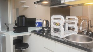 Una cocina moderna con pileta de acero inoxidable, tetera, cafetera y refrigerador compacto.