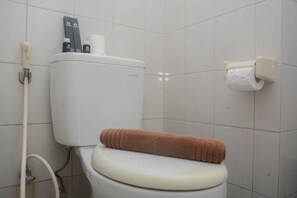 Eine Toilette mit Handtuch auf dem Sitz, einem Toilettenpapierhalter und einem Bidet-Sprüharm an der Wand.