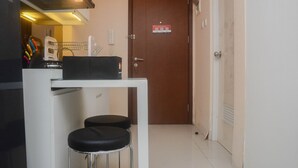 Cocina compacta con microondas, una mesita y dos taburetes. Se ve una puerta con un cartel en el fondo.