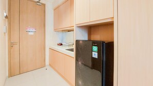 Une cuisine de taille réduite, avec des meubles de rangement en bois, un réfrigérateur noir et un petit plan de travail.